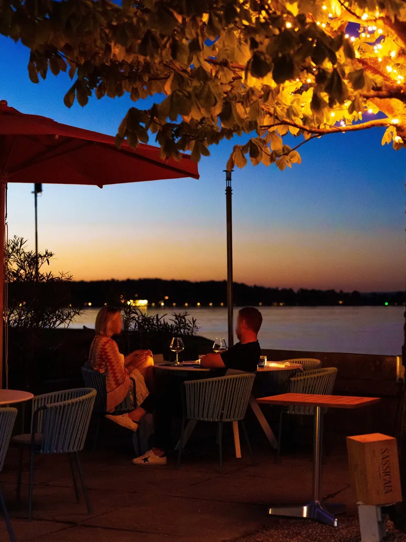 Abend unter der Platane mit Lichterkette, Gäste am Tisch über dem See