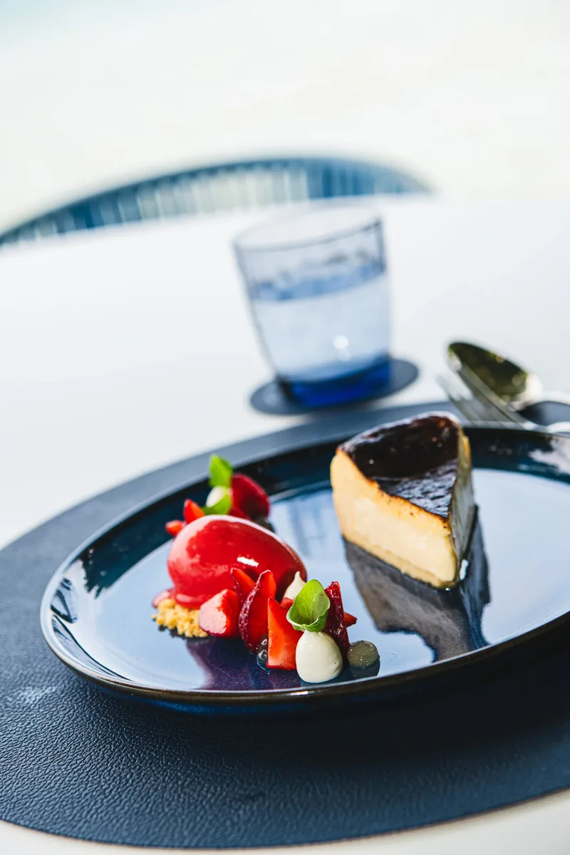 Dessert mit Beeren auf einem blauen Teller, dahinter ein Wasserglas