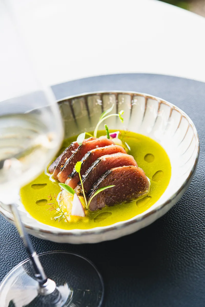 Fisch in grüner Sauce in einer gerippten Schale, daneben ein Weinglas